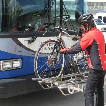A person loading a bicycle onto the bicycle rack on the front of a bus