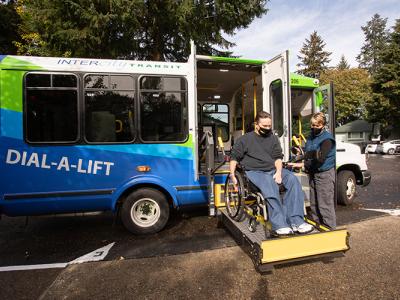 Image of dial-a-lift van with driver helping a passenger in a wheelchair enter van