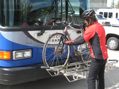 A person loading a bicycle onto the bicycle rack on the front of a bus
