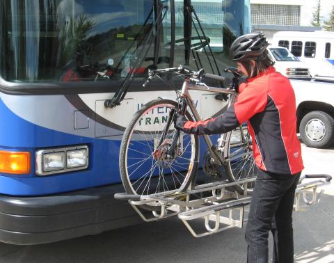 A person loading a bicycle onto the bicycle rack on the front of a bus